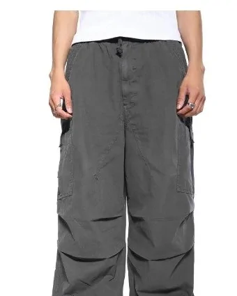 Loose grey cargo trousers with knee pleats and drawstring hems, worn