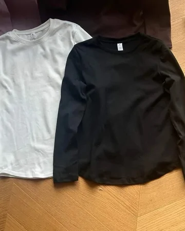 Plain white and black long-sleeve tees laid on a wooden floor